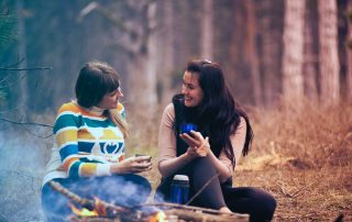 Par de amigas conversando en medio del bosque con un café en la mano